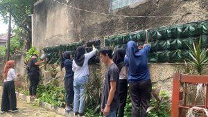 Mahasiswa sedang menanam vertikal garden di tembok sekitar laboratorium